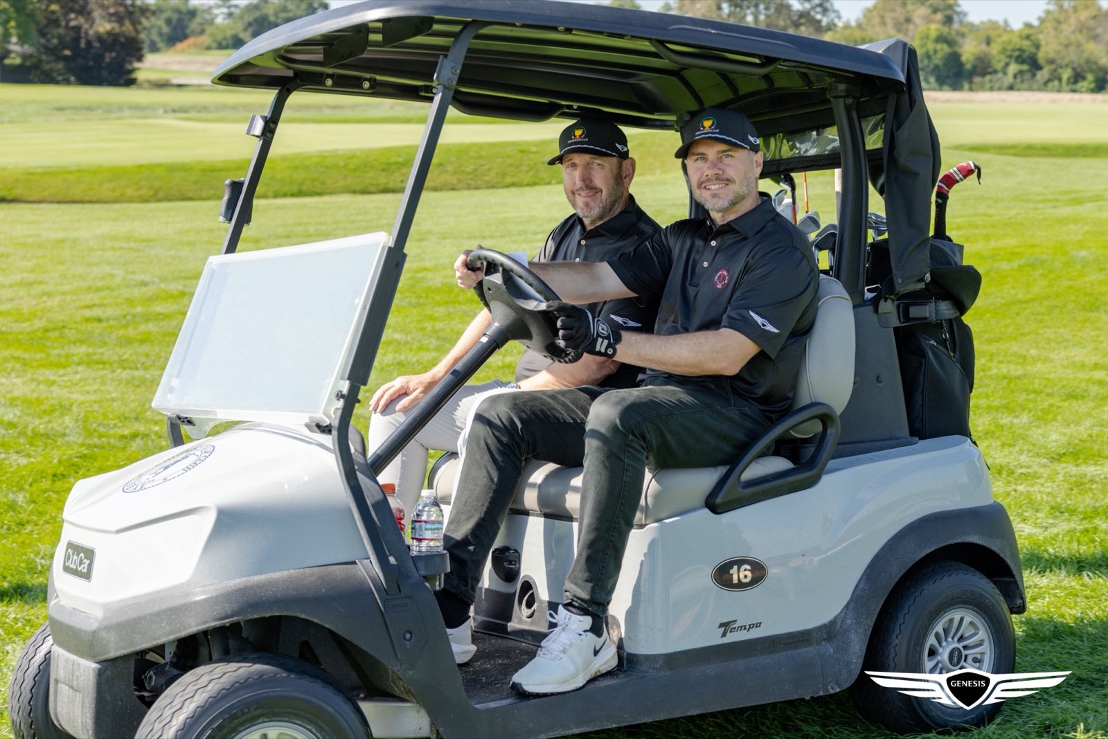 Two Genesis Presidents Cup guests in a golf cart wearing Presidents Cup caps