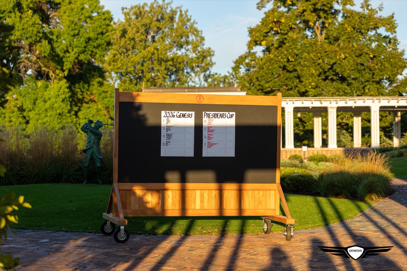 A Genesis Presidents Cup pairings board standing outside the clubhouse at golden hour