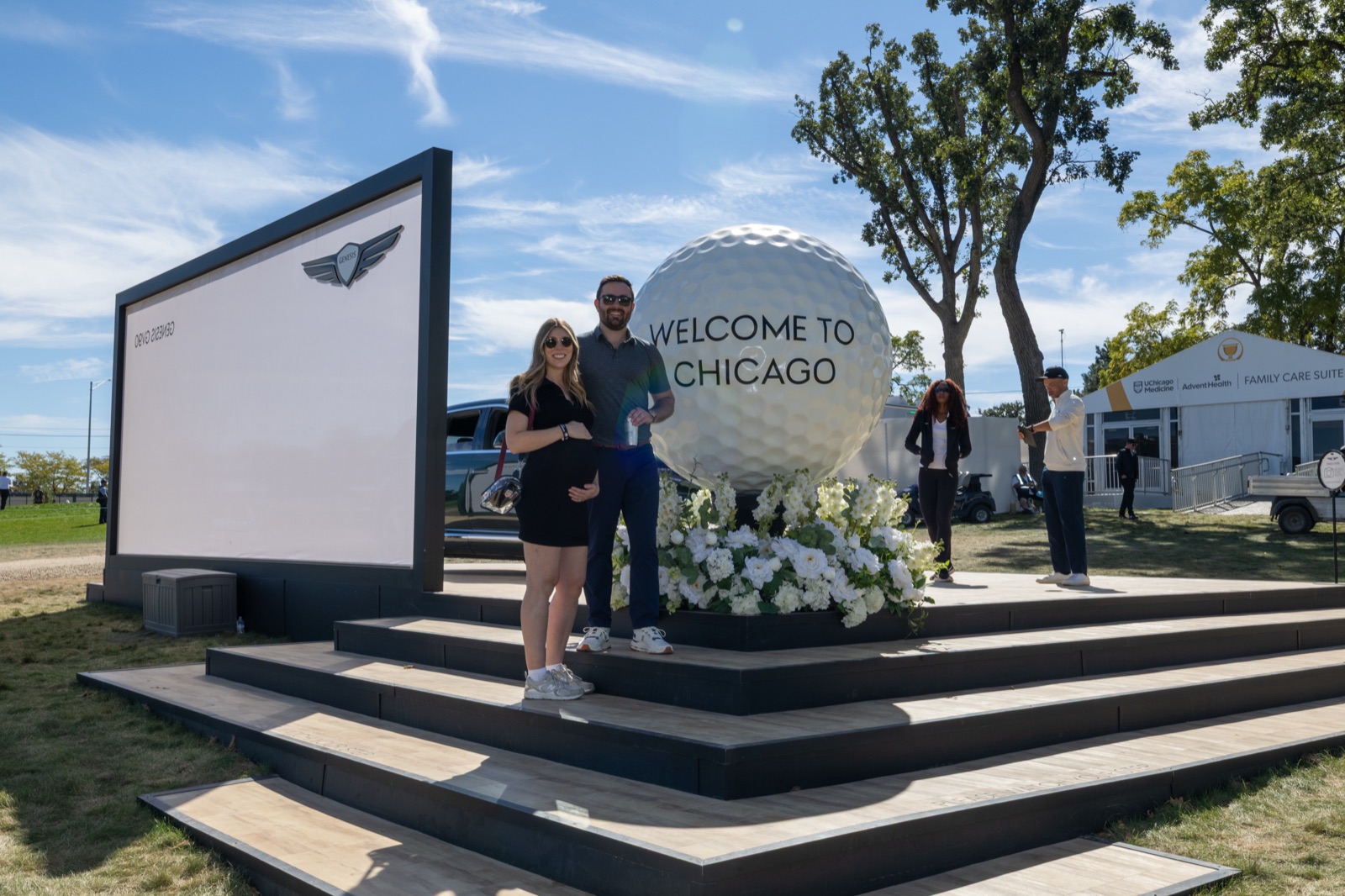 Two guests on the steps of a giant Welcome to Chicago golf ball beside a Genesis display at Medinah