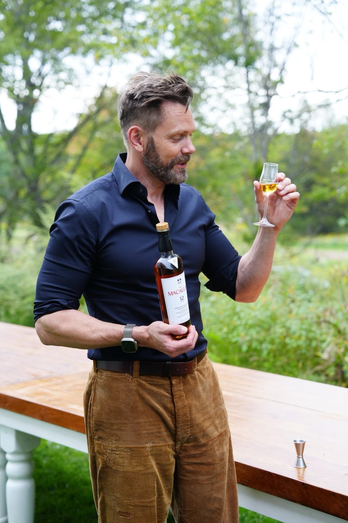 A host holding a bottle of The Macallan 12 and a tasting glass outdoors at INNESS