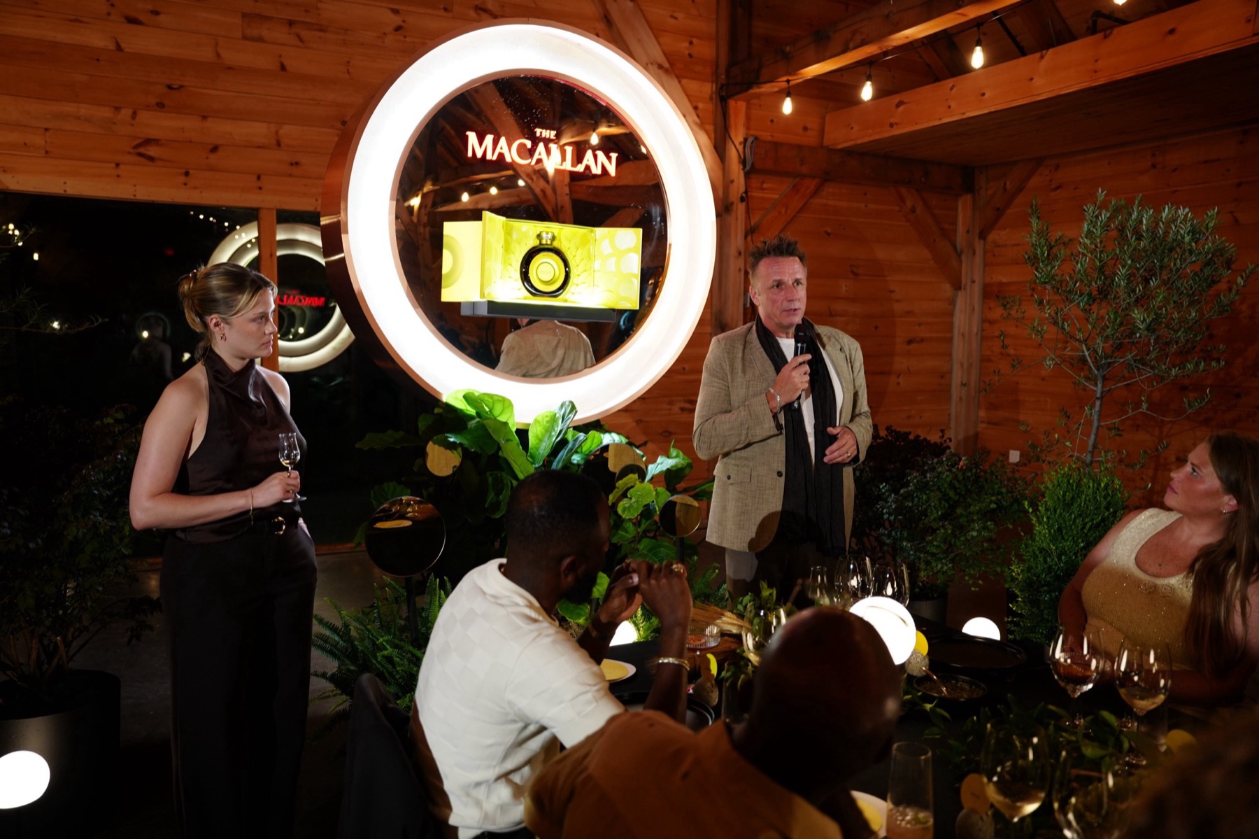 A host from The Macallan introducing dinner beside the illuminated The Macallan sign