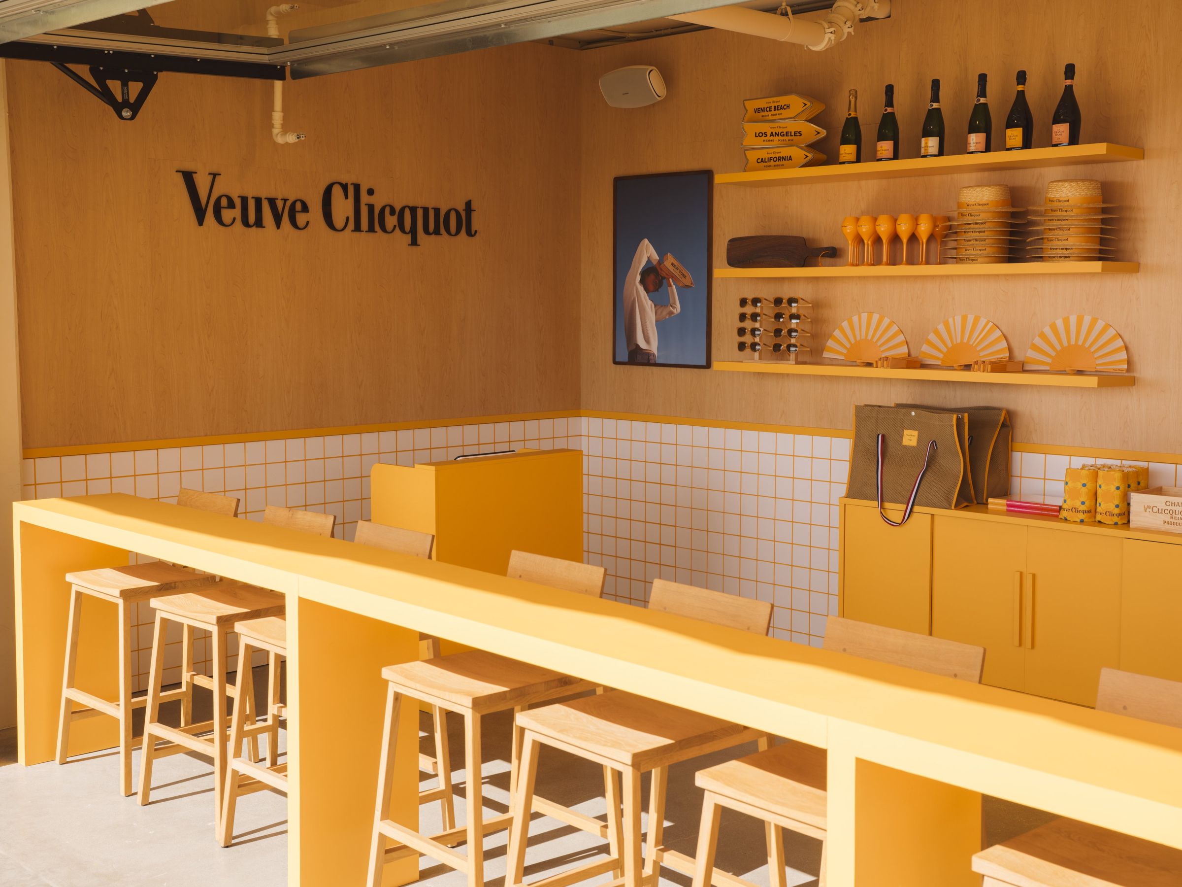 The Veuve Clicquot bar at Club Solaire in Venice Beach, with yellow counters, wooden stools and branded shelves