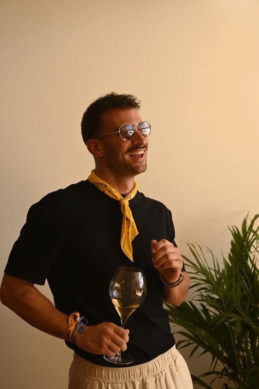 A smiling Club Solaire guest in sunglasses and a yellow bandana holding a glass of champagne