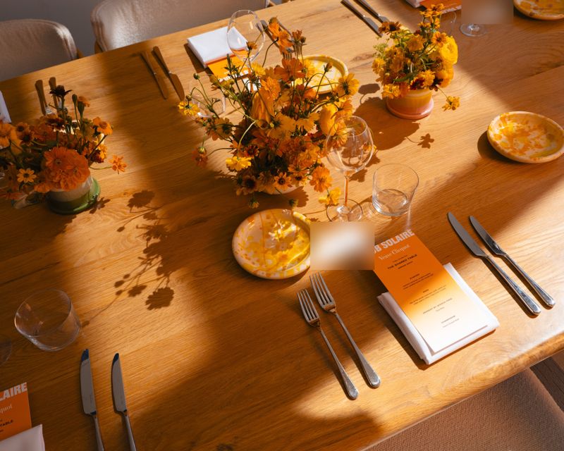 A Club Solaire table set with orange flowers, menus and glassware
